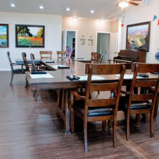 A spacious dining room with wooden chairs and tables, adorned with colorful artwork and a piano.