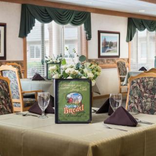 A neatly set dining table in a restaurant with floral centerpiece and menu display.