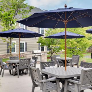 A patio area with tables and chairs under large blue umbrellas, set in a garden setting.