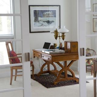 A home office setup with a wooden desk, laptop, and lamp, framed by glass doors.