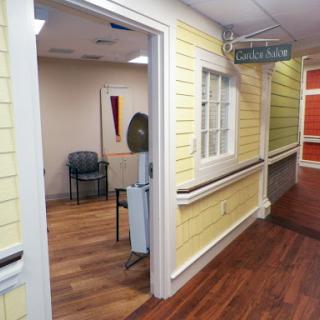 A view of a hospital corridor featuring yellow walls and a wooden floor, leading to a waiting area.