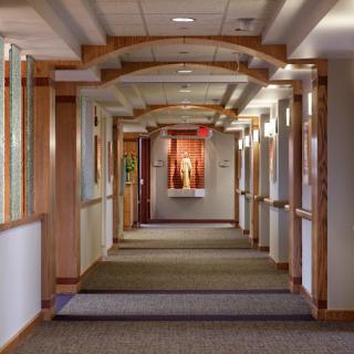 A hallway with wooden beams and carpet, featuring decorative lighting and artwork at the end.