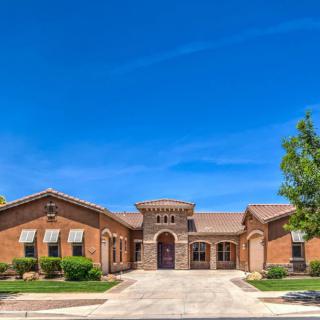 A large suburban brick house with a landscaped front yard under a clear blue sky.