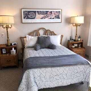 A cozy bedroom with a neatly made bed, flanked by two nightstands and elegant lamps, and artwork hanging above.