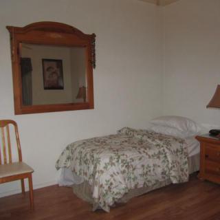 A simple bedroom with a single bed, wooden mirror, and minimal decor.