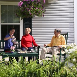 Three people enjoying a relaxing time together on a porch surrounded by flowers.