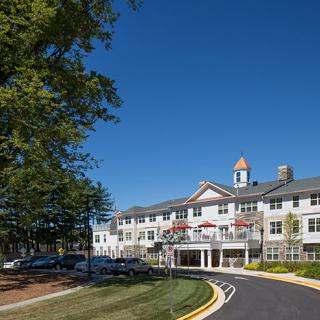 A residential building with multiple levels, surrounded by trees and under a clear blue sky.