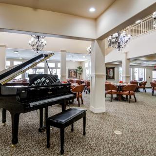A spacious interior with a grand piano and dining area featuring elegant lighting and carpeted floors.