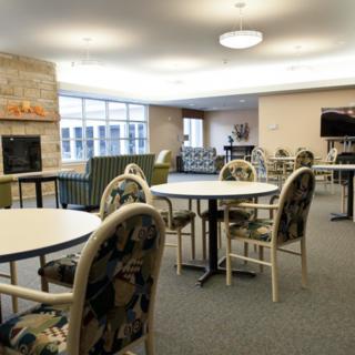 A spacious lounge area with tables and chairs, featuring a fireplace and large windows.