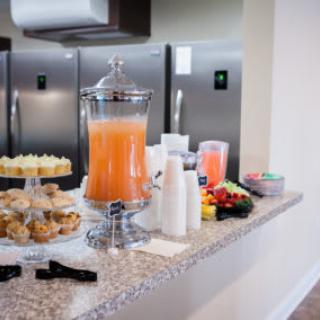 A countertop with a variety of refreshments, including a juice dispenser, pastries, and a fruit platter.