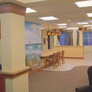 A cozy interior space featuring a mural, seating area with chairs and overhead lighting, and large windows with curtains.