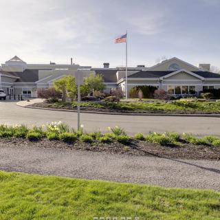 A large building with a flag on top, surrounded by landscaping and a clear sky.