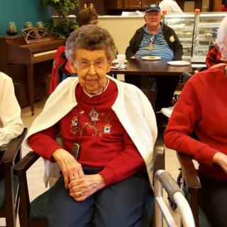 A group of elderly people gathered indoors, some seated in wheelchairs.