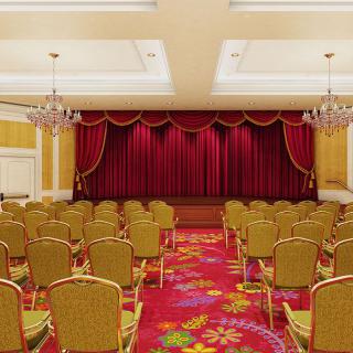 Empty auditorium with arranged seating and a stage with red curtains.
