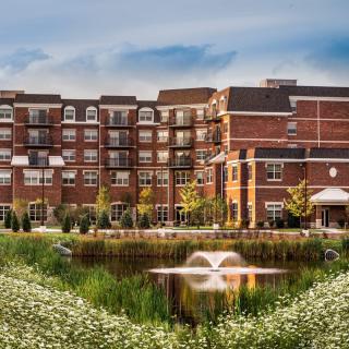 A residential building with a pond and fountain in front, surrounded by flowers and landscaping.
