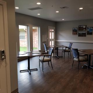 A cozy dining area featuring several tables and chairs, illuminated by ceiling lights and natural light from the windows.