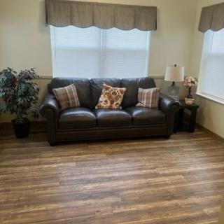 A cozy living room with a leather sofa and decorative pillows, complemented by wood flooring and natural light.