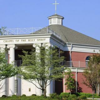 A church building featuring classical architecture with a cross on top and surrounded by trees.
