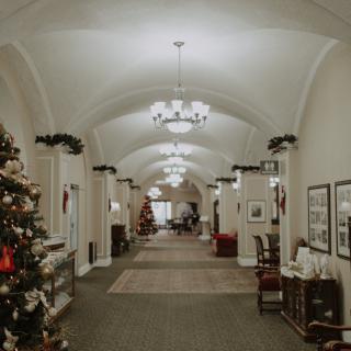 A decorated hallway with Christmas trees and chandeliers under an arched ceiling.