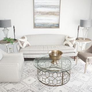 A modern living room with neutral tones featuring a sleek sofa, glass coffee table, and coordinating lamps.