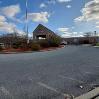 A view of a commercial building with a landscaped parking area under a partly cloudy sky.