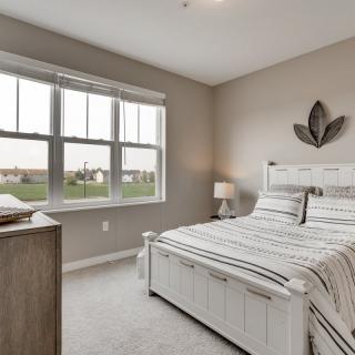 A modern and minimalist bedroom with neutral tones and ample natural light streaming through the window.