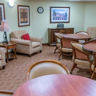 A comfortable lounge area with multiple tables and chairs, decorated with framed pictures and a sideboard.