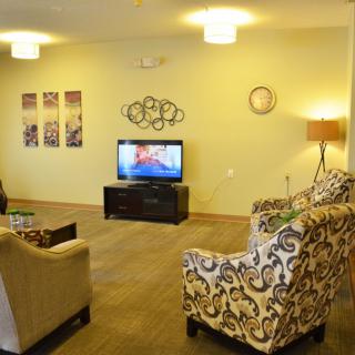 A cozy living room with patterned armchairs, a television, and decorative wall art.
