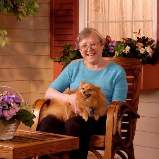 A woman smiles while sitting on a porch with a dog on her lap.