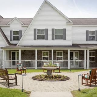 A charming two-story house with a stone and white siding exterior, featuring a front porch and an inviting garden area with outdoor seating.
