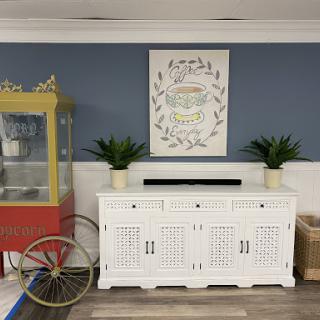 A cozy and stylish interior featuring a white cabinet, botanical artwork, and a vintage popcorn cart against a blue wall.
