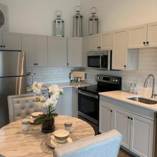 A modern kitchen with stainless steel appliances, white cabinetry, and a cozy dining area featuring a marble table and an orchid centerpiece.