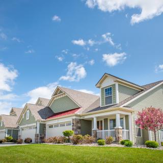 A row of suburban houses with well-maintained lawns under a clear blue sky.