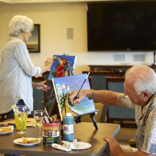 Two seniors engaged in a painting activity, working on colorful canvases during an art class.