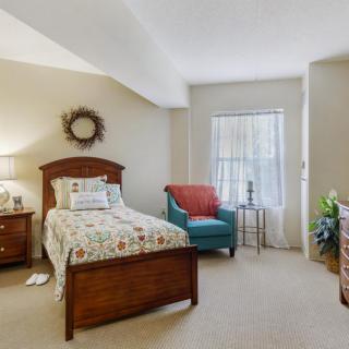 A cozy bedroom with a single bed, armchair, and window.