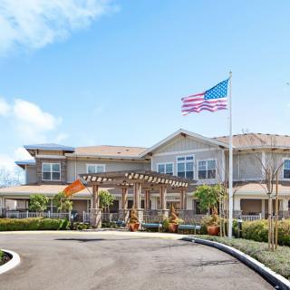 A residential building with an American flag at the entrance surrounded by landscaped greenery.