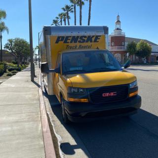 A Penske moving truck parked on a sunny street lined with palm trees.