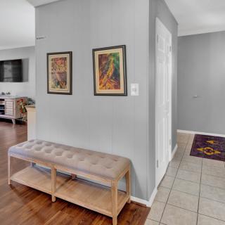 A modern hallway featuring a cushioned bench, two framed artworks on grey walls, and a combination of wooden and tiled flooring.