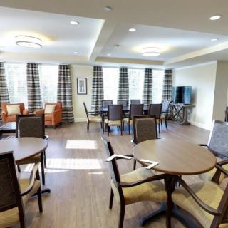 A modern dining area with multiple tables and chairs, featuring large windows with curtains and a TV.