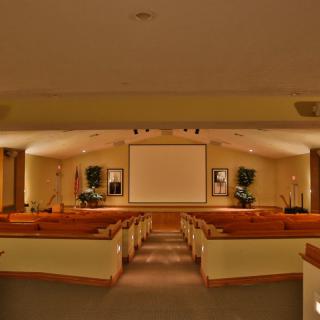 A church sanctuary interior with rows of pews leading to an altar and a large projector screen.
