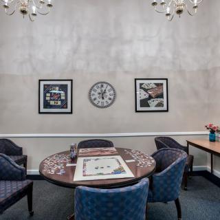 A cozy meeting room with a round table surrounded by chairs, decorated with artwork and a wall clock.