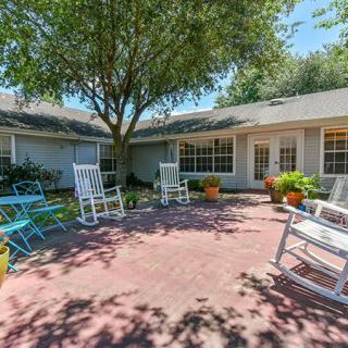 A sunny patio area with rocking chairs, a tree, and various plants creates a relaxing outdoor space.