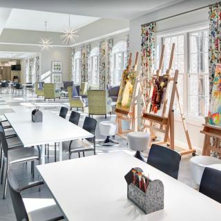 A bright and airy art studio with tables, chairs, and easels set up for painting.