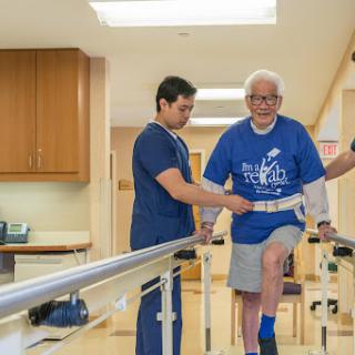 A healthcare professional assists an elderly patient during a physical therapy session in a rehabilitation facility.