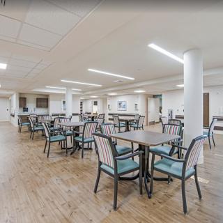 A spacious dining room with multiple tables and chairs, featuring bright lighting and a wooden floor.