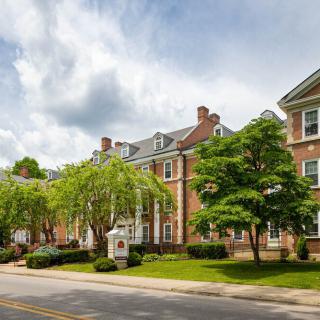 A picturesque brick building with a manicured lawn and trees lining the street under a cloudy sky.
