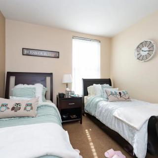 A cozy bedroom with two twin beds, featuring decorative pillows, a nightstand with a lamp, and a wall clock.