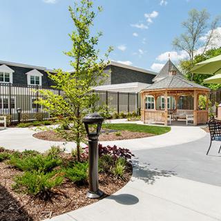 A well-maintained garden with a gazebo and outdoor seating area surrounded by lush greenery and a modern building in the background.
