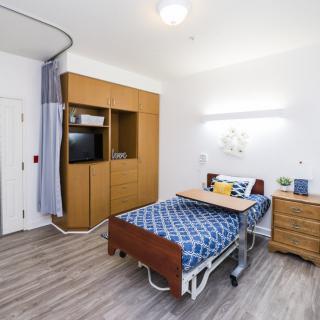 A modern hospital room with a single bed, television, and wooden furniture.