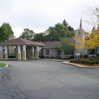 A view of a building with an entrance and driveway surrounded by trees.